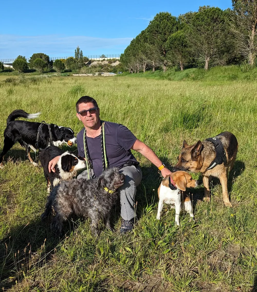 Mike, responsable de la pension Chez Tonton Mike, accroupi dans un pré, entouré de cinq chiens